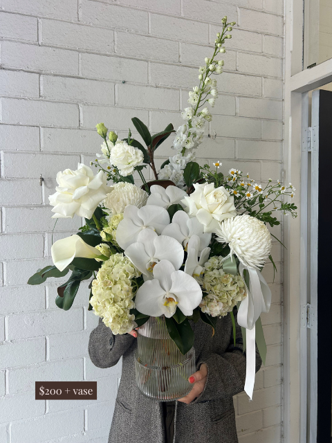 Bouquet of white flowers with a vase held by a person against a light gray brick wall.