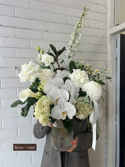 Bouquet of white flowers with a vase held by a person against a light gray brick wall.