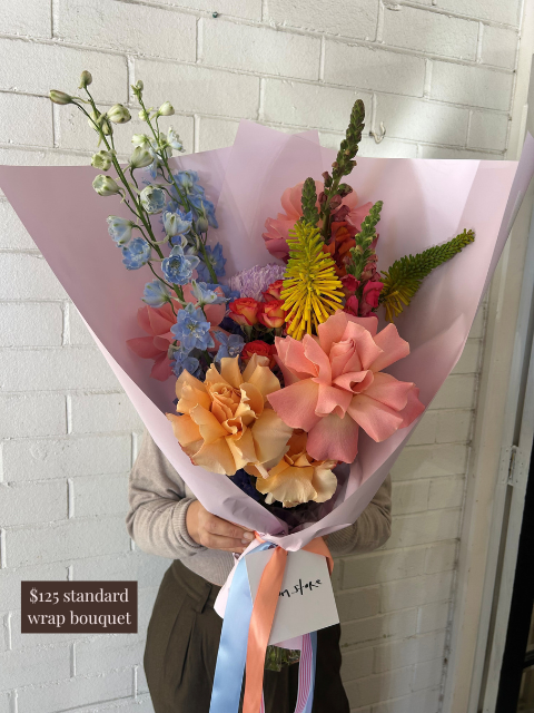 Person holding a colorful bouquet of flowers against a white brick wall.