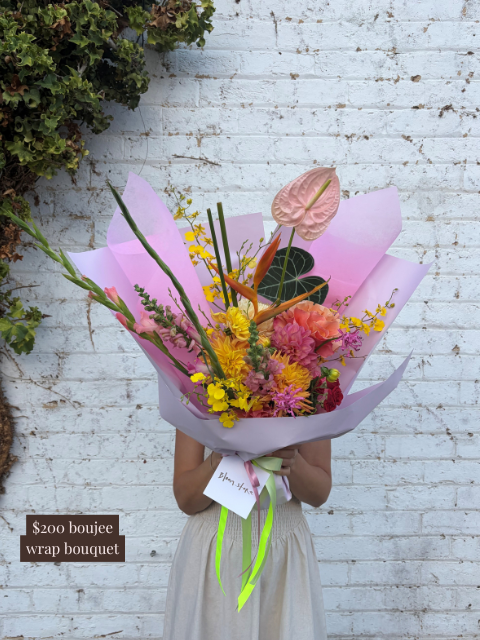 Person holding a colorful bouquet of flowers against a light brick wall.