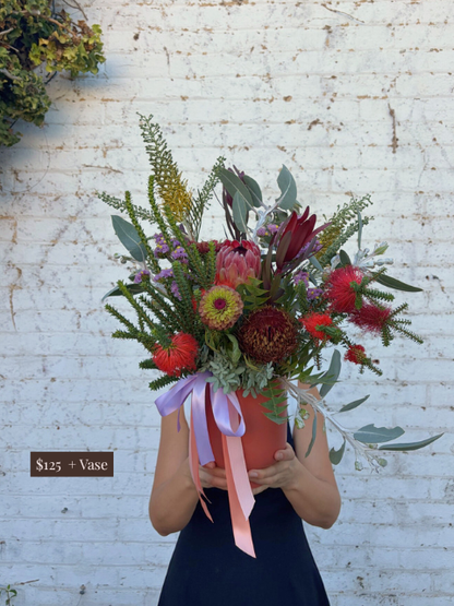 Person holding a vibrant bouquet of flowers against a white brick wall.