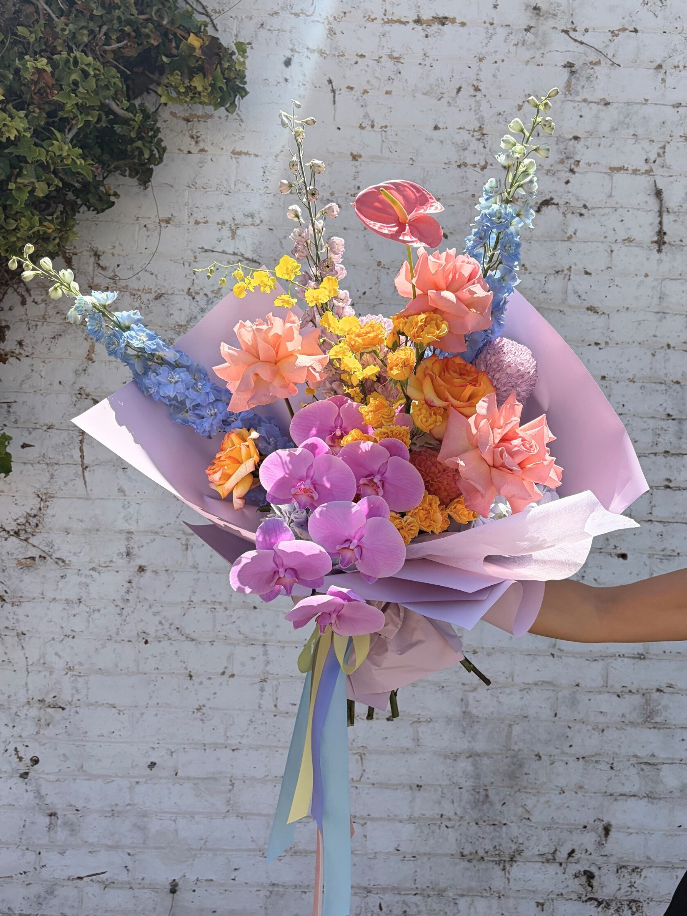 Bouquet of flowers with pink orchids against a white brick wall.