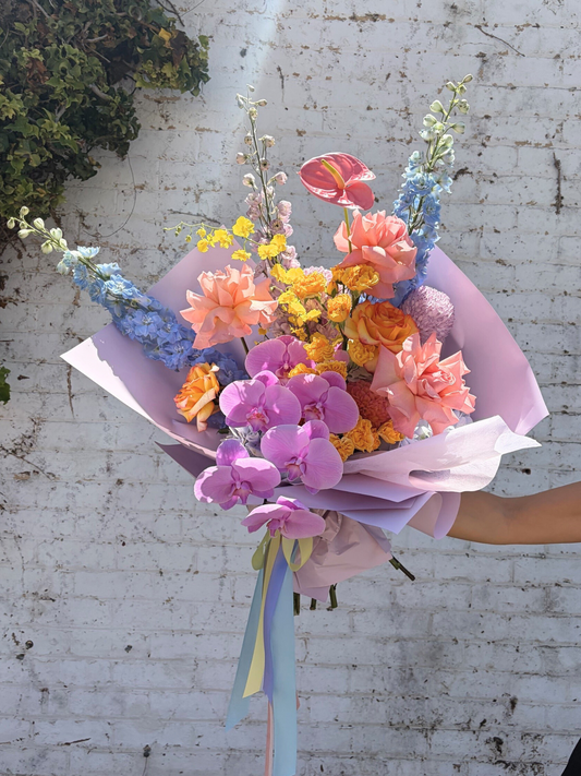 Bouquet of flowers with pink orchids against a white brick wall.