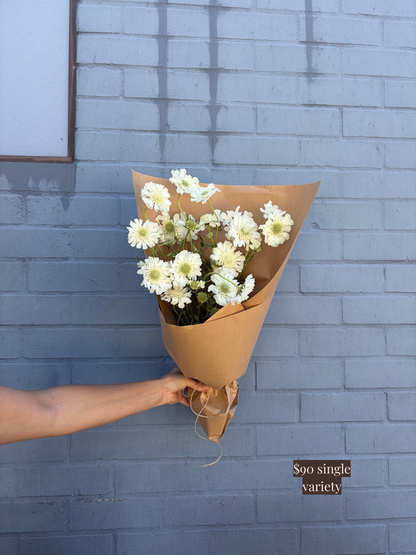 Bouquet of white flowers wrapped in brown paper held against a blue brick wall.