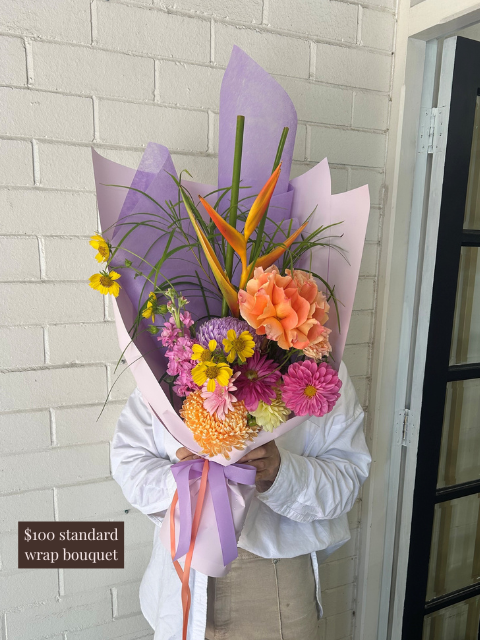 Person holding a colorful bouquet of flowers against a white brick wall.